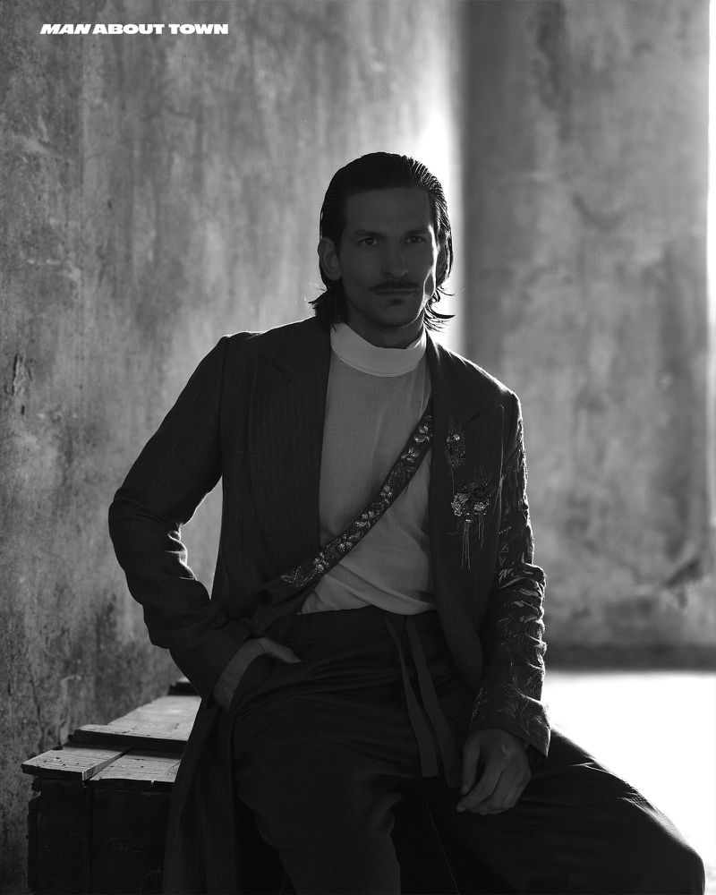 Monochrome portrait of a middle-aged male model wearing a suit, seated indoors with a neutral facial expression and soft lighting.