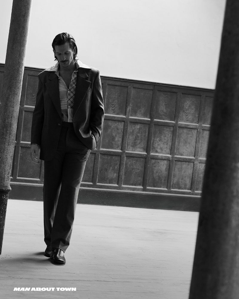 Monochrome fashion editorial image featuring a male model walking outdoors in a tailored suit and patterned shirt.