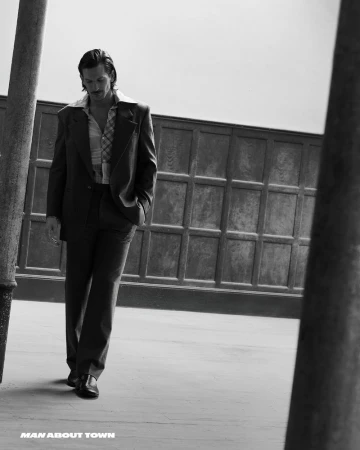 Monochrome fashion editorial image featuring a male model walking outdoors in a tailored suit and patterned shirt.