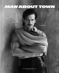 Model Jarrod Scott with folded knit sweater and leather pants against a textured concrete wall for Man About Town.