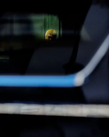 A person with dyed blonde hair framed through a dark window reflection with a blue accent bar.