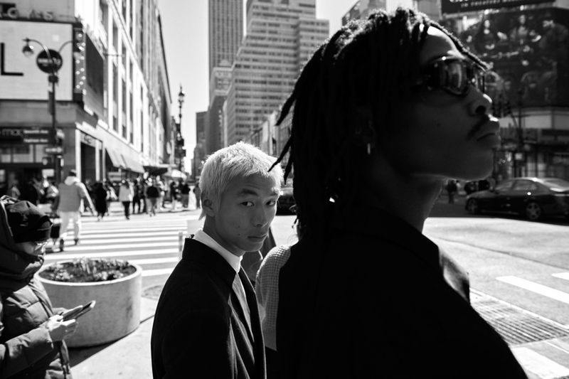 Black and white street editorial featuring two male models in a busy urban setting with skyscrapers and traffic.