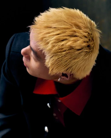 High-angle portrait of a man with textured blonde hair wearing a dark jacket and red shirt for Rouge Fashionbook.