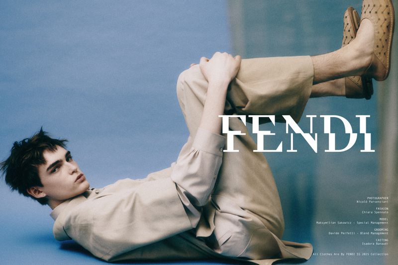 Fashion portrait of a male model wearing a light tan, long-sleeved shirt and pants, lying on a blue surface with the Fendi logo.
