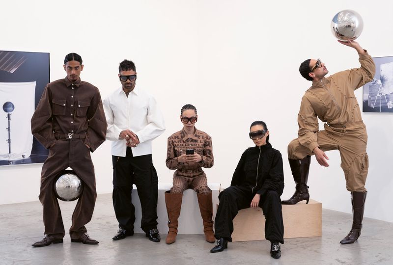 Five people wearing stylish jumpsuits and eyewear strike poses in a photo studio with disco balls and photographic prints on the wall.