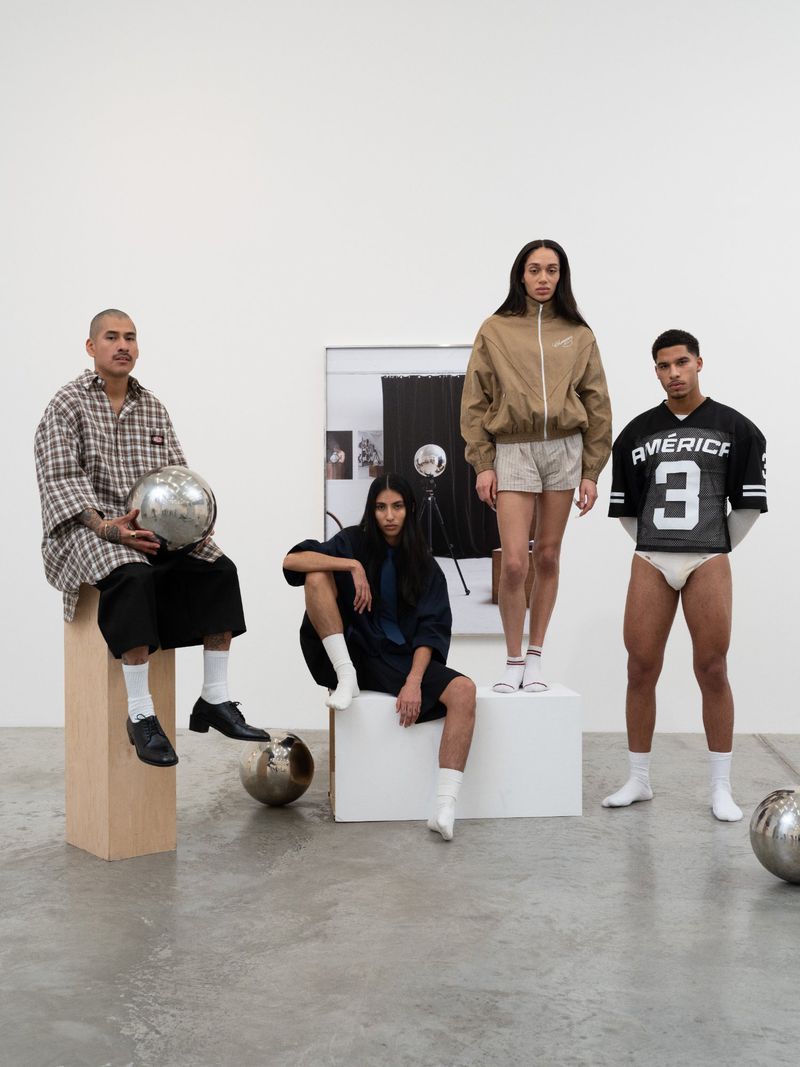 Group of four diverse models in casual fashion posing in a minimalist studio setting with silver sphere props and geometric platforms.
