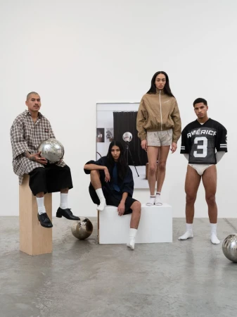 Group of four diverse models in casual fashion posing in a minimalist studio setting with silver sphere props and geometric platforms.