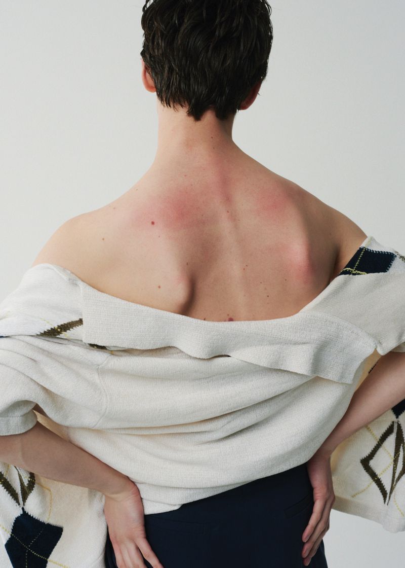Rear view of a person wearing an off-the-shoulder patterned white sweater against a plain white background