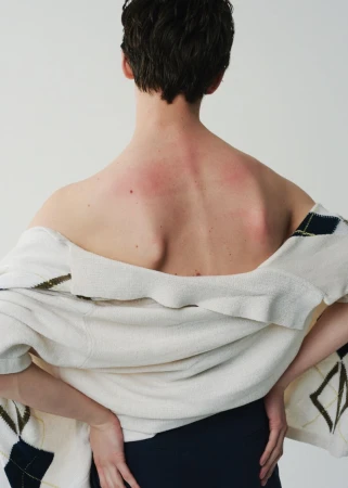 Rear view of a person wearing an off-the-shoulder patterned white sweater against a plain white background