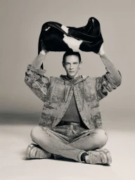 Man sitting cross-legged holding a black and white patterned bag above his head in a studio setting