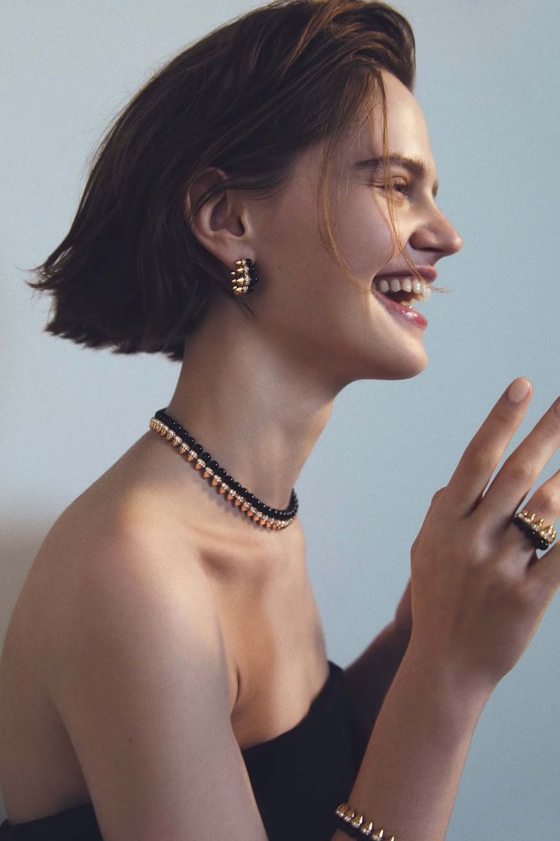 Close-up profile of a woman with short brown hair laughing, wearing jewelry, including a gold and black choker necklace.