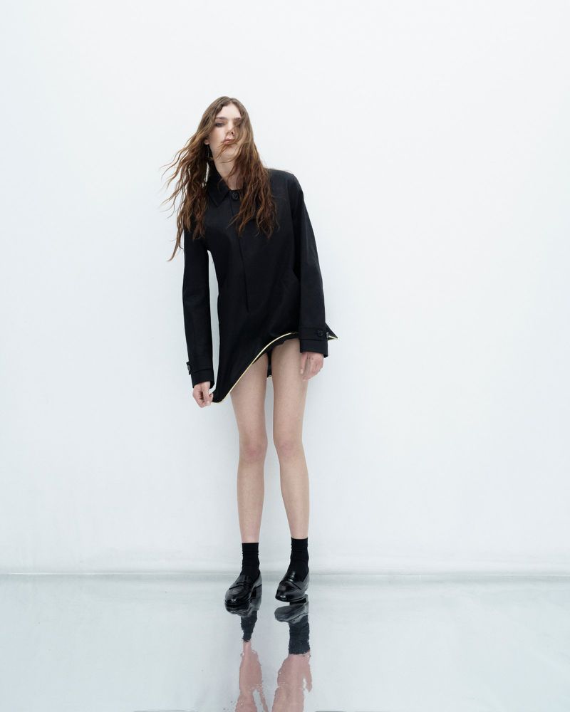 Model in black coat with long hair blowing against a plain white background