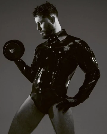 Man wearing a black latex shirt holding a dumbbell against a neutral background