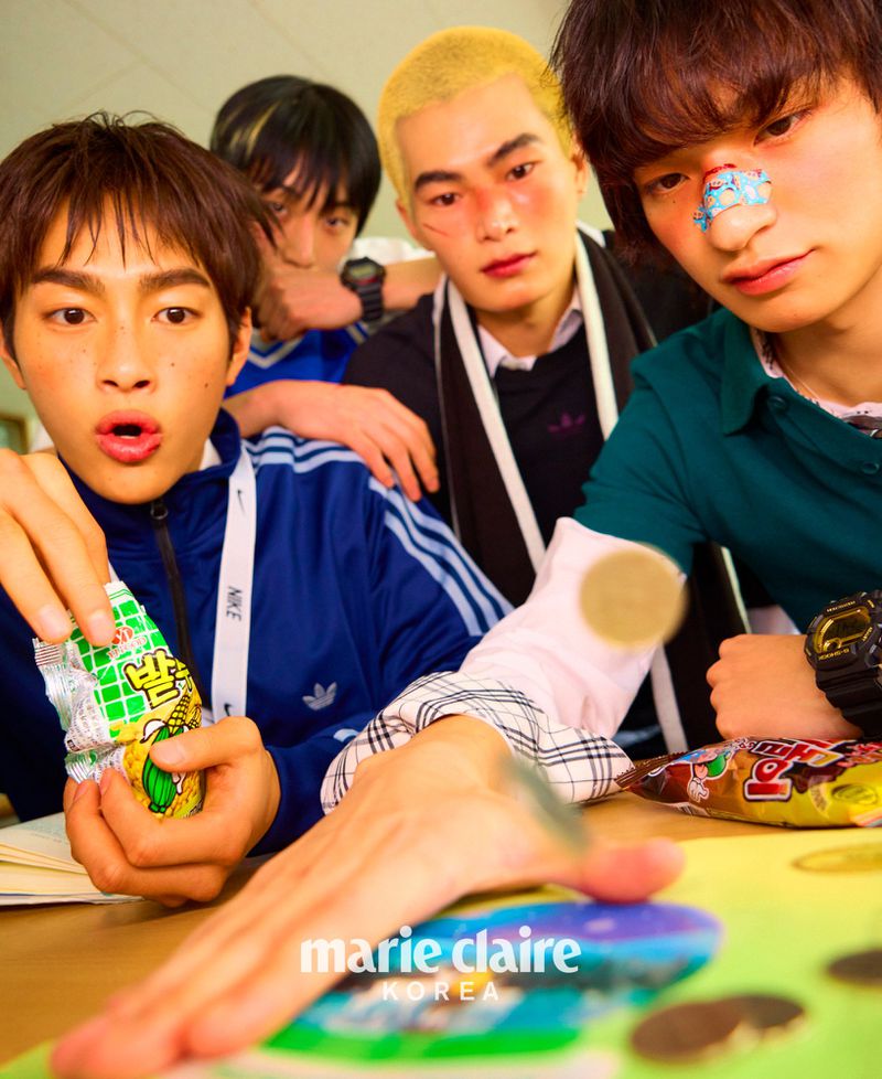 High-angle shot of five young Asian adults grouped indoors, some at a table with snack foods, magazine, and bright studio lighting.