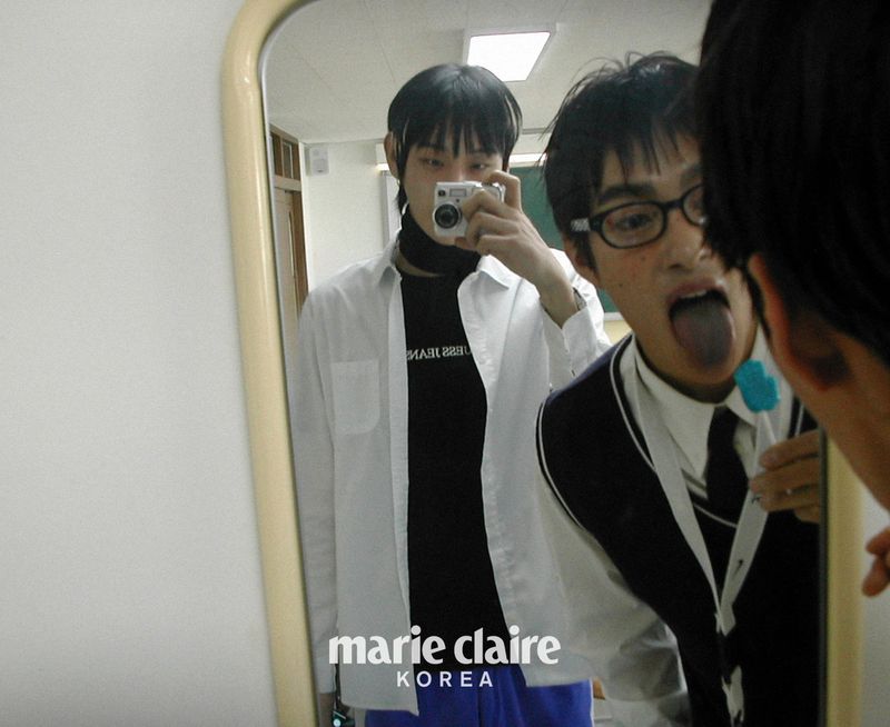 Two young men in a mirror selfie; one holding a camera, the other in a school uniform with his tongue out and a blue lollipop.