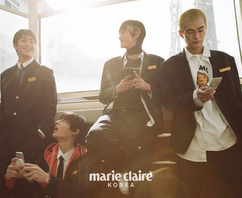 Group of young Asian men in school uniforms holding phones, posing indoors with bright lighting. Marie Claire Korea logo is visible.