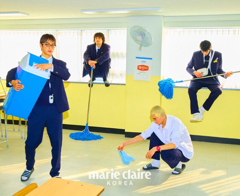Four young adult males in school uniforms in a classroom, creatively posing with cleaning supplies and equipment for Marie Claire Korea.