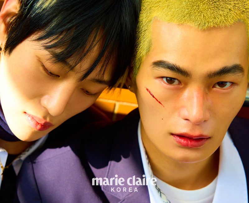 Two young Asian men pose for a fashion editorial, with one resting his head on the other's shoulder in a close-up studio shot.