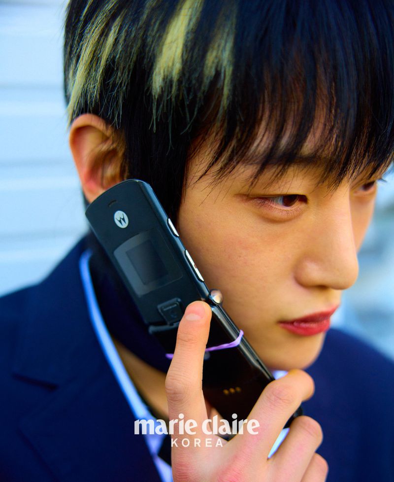 Close-up of an adult male using a black Motorola Razr flip phone, with a blue jacket and a Marie Claire Korea logo visible.