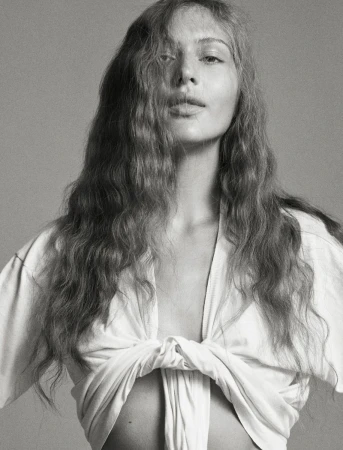 Model Angelina Kendall in a tied white t shirt with long wavy hair against a grey seamless background