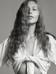 Model Angelina Kendall in a tied white t shirt with long wavy hair against a grey seamless background