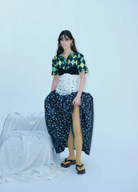 Full-length shot of a woman in a patterned crop top and long skirt, striking a pose in a white photo studio with soft, diffused lighting.