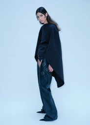 Model wearing dark cape-style top and studded leather chaps against a pale neutral background for Heroine Magazine editorial.