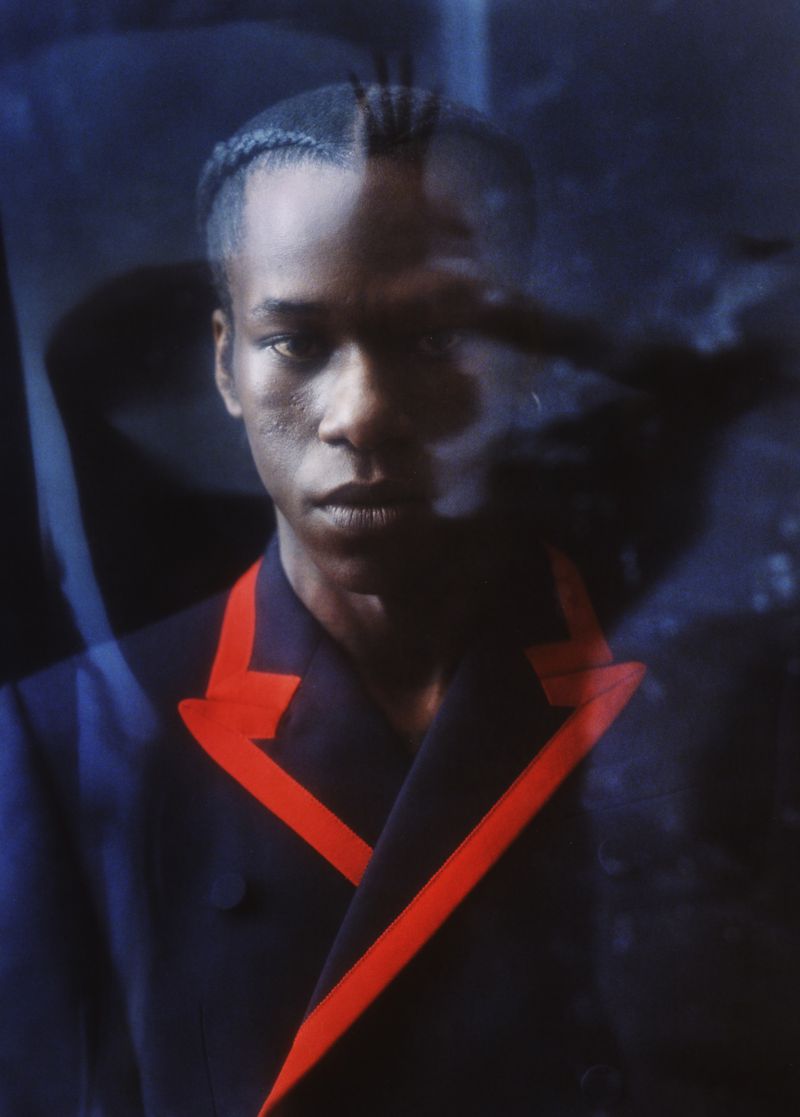 Portrait of a young Black man in a suit with red details, dark hair, and light skin, captured in a studio setting with a diffused lighting.