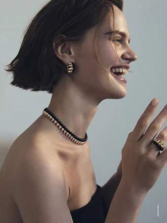 Smiling woman in black strapless top wearing jewelry including earrings, a ring, and a beaded choker necklace in studio setting.