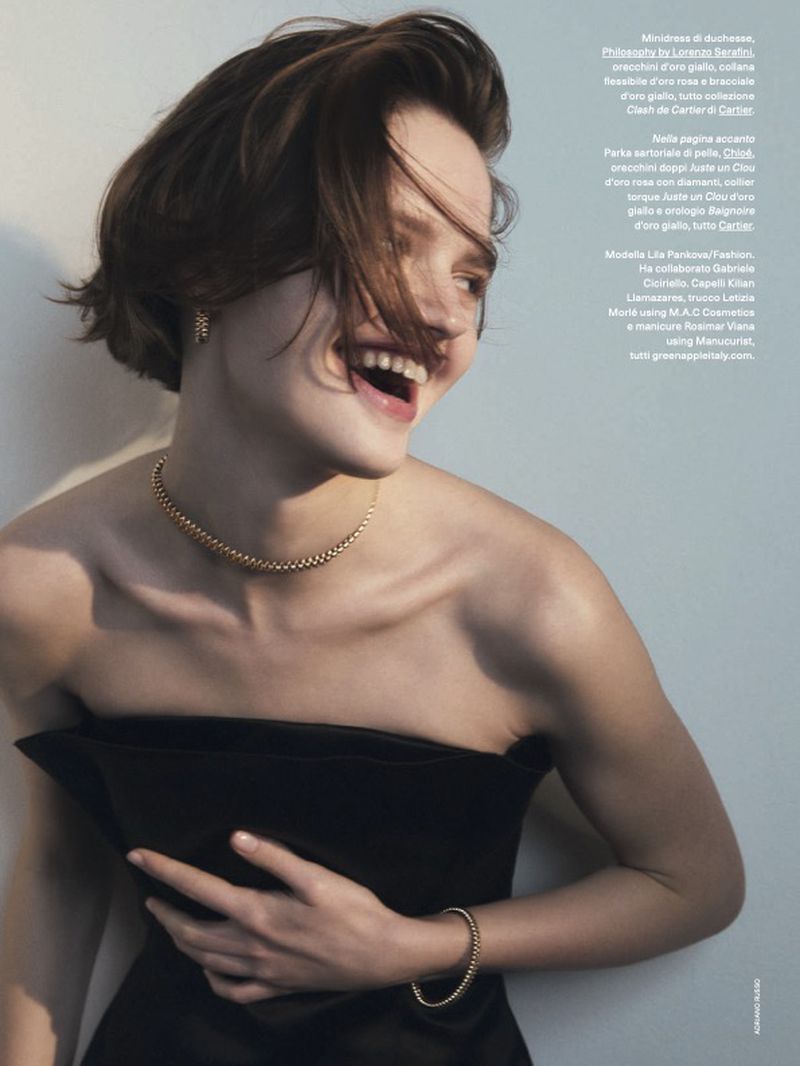 A smiling young woman poses in a strapless black dress with golden jewelry. Soft, natural light highlights her joyful expression.