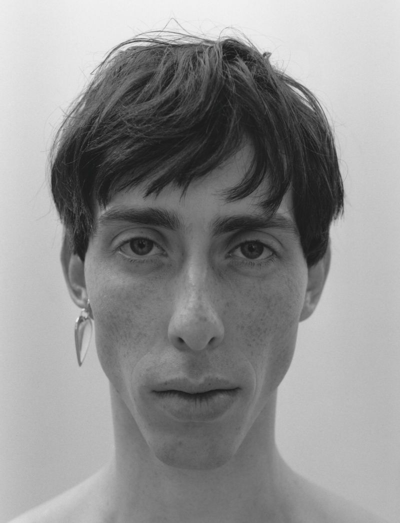 Close-up monochrome portrait of a young man with dark hair and a single earring against a light background for The Greatest Magazine