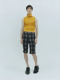 Model wearing a mustard yellow sleeveless turtleneck top and plaid patterned shorts against a neutral white background.