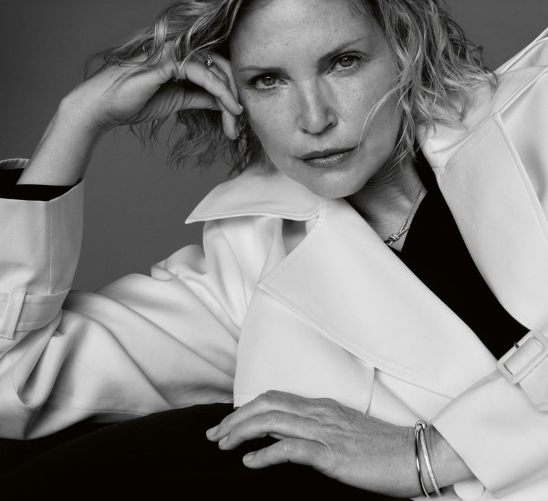 Black and white portrait of a mature woman with blond hair, wearing a white coat. She is resting her head on her hand.