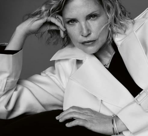 Monochrome portrait of a woman resting her hand near her temple, wearing a white collared coat and dark top.