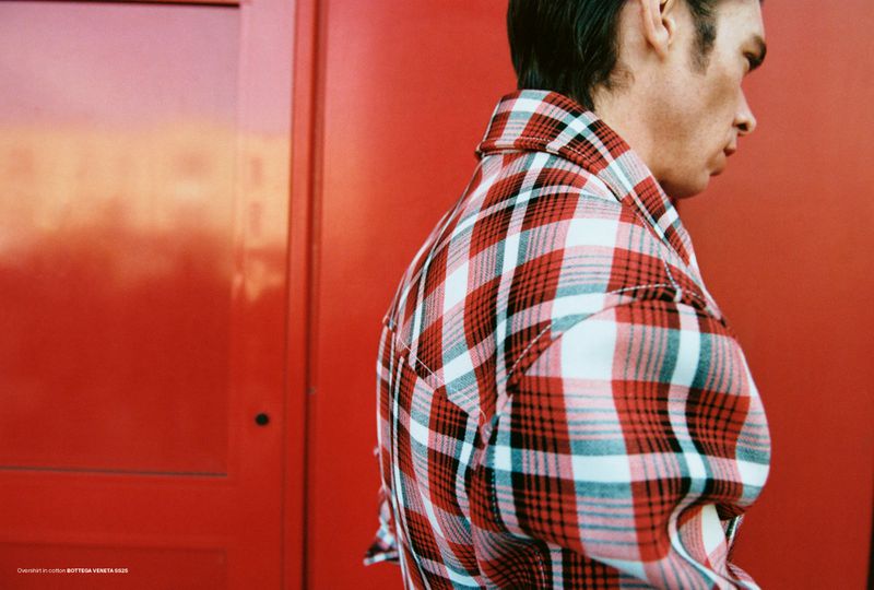 Close-up profile of model Cole Mohr wearing a red and white plaid overshirt against a vibrant red background for AnOther Man Magazine.