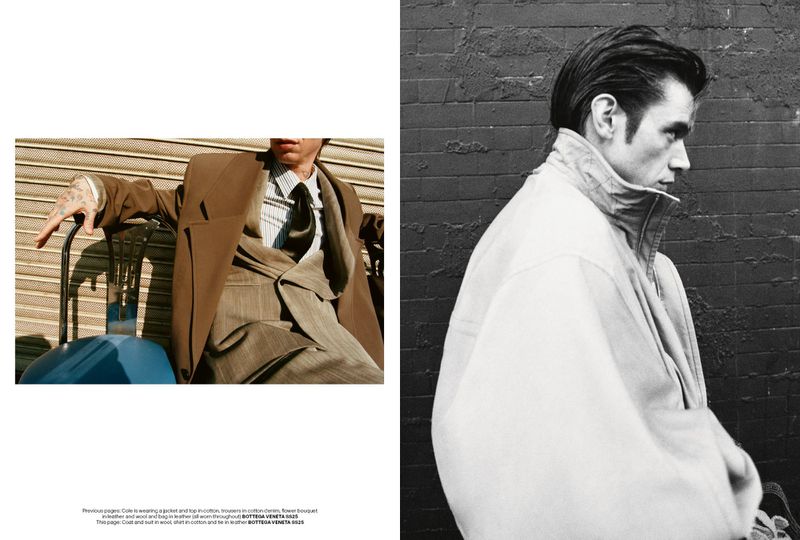 Editorial fashion shot of a tattooed man in a brown suit sitting on a chair next to a blue bag against a textured metal wall, in monochrome.