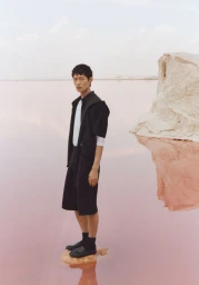 Model standing on a rock in shallow pink water wearing a black outfit for Zara technical wardrobe