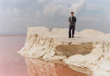 Model standing on a pale earth formation next to pink water under a cloudy sky for Zara Technical wardrobe