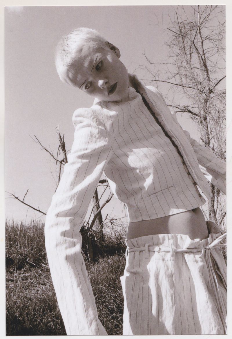 Monochrome portrait of a woman with short blonde hair wearing a pinstripe suit, outdoors on a sunny day, shot from a low angle.