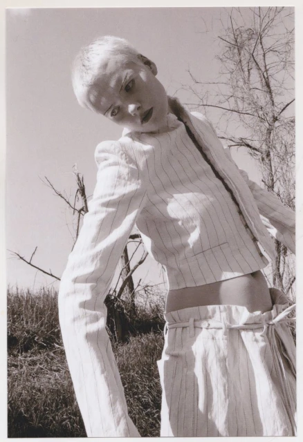 Monochrome portrait of a woman with short blonde hair wearing a pinstripe suit, outdoors on a sunny day, shot from a low angle.