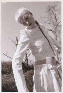 Model with short blonde hair wearing a striped jacket outdoors against bare trees and sky