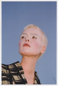 Portrait of a model with short blonde hair wearing a patterned top against a clear blue sky background