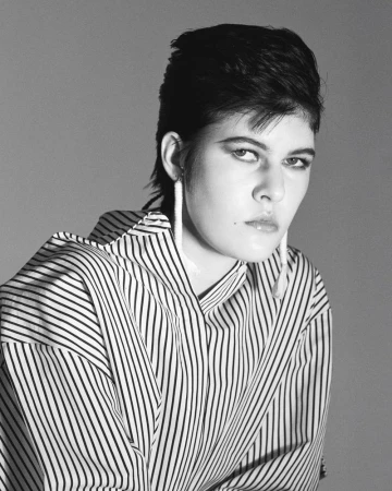 Model Rachel Goff in a black and white striped shirt with long earrings against a grey studio backdrop.