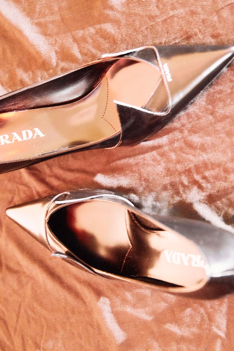 Elegant metallic bronze Prada stiletto high heels on a crushed velvet background, fashion-forward footwear.