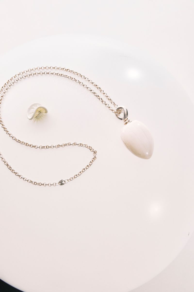 Elegant silver chain necklace with an oval white pendant on a white background, jewelry photography. Minimalist fashion accessory.