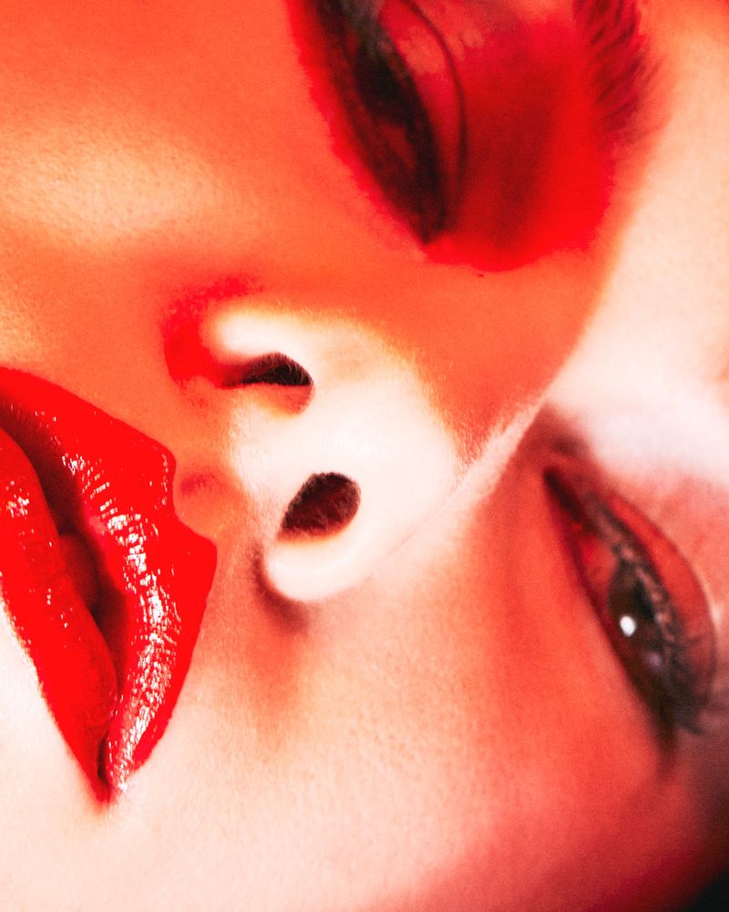 Close-up portrait of an adult female face with red lipstick, dramatic makeup, and contrasting light. Beauty and fashion concept.
