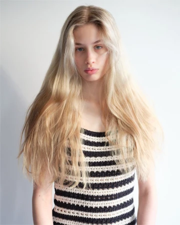 Portrait of a young blonde woman wearing a black and white striped top against a plain light wall.
