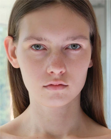 Close-up portrait of model Sanique Dill with long brown hair and neutral expression against a plain background