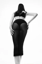 Model Aylah Peterson facing away wearing black undergarments and mesh tights against a plain white seamless studio background.