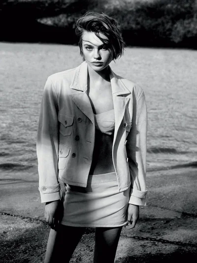 Monochrome fashion portrait of model Anne Boomgaart wearing a tailored jacket and skirt outdoors near water for Telva.